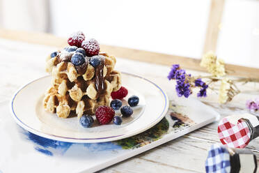 Teller mit einem Stapel goldener Waffeln, garniert mit frischen Beeren und Schokoladenüberzug auf dem Tisch - ADSF14346