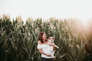 Happy woman with dog at cornfield during sunset - EBBF00672