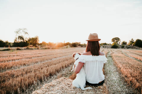 Woman and dog sitting on straw bale during sunset stock photo