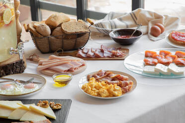 Blick von oben auf den gemütlich gedeckten Tisch mit Spiegeleiern und Speck, Lachs, Käse und Gebäck zu Hause - ADSF14396