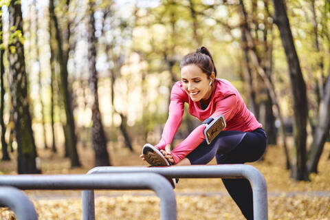 Young female jogger stretching her leg on bicycle stand in autumn forest stock photo