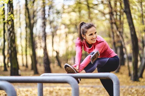 Junge Joggerin streckt ihr Bein auf einem Fahrradständer im Herbstwald, lizenzfreies Stockfoto