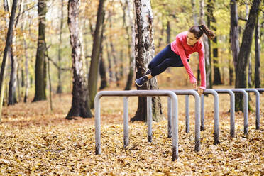 Junge Joggerin springt über Fahrradständer im Herbstwald - BSZF01695