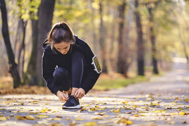 Young woman tying her running shoe - BSZF01699