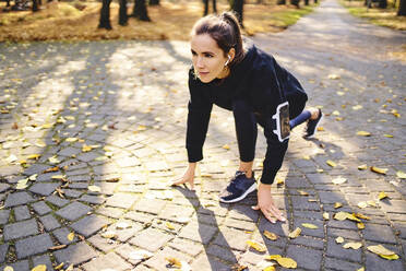 Junge Frau in Startposition auf dem Weg im Herbstwald - BSZF01701