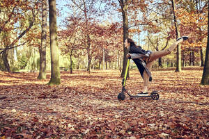 Glückliche junge Frau fährt Roller im Herbst Wald - BSZF01710