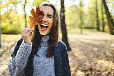 Young laughing woman holding autumn leave on her eye - BSZF01711