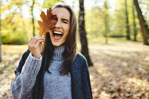 Junge lachende Frau hält Herbstlaub auf ihrem Auge - BSZF01711