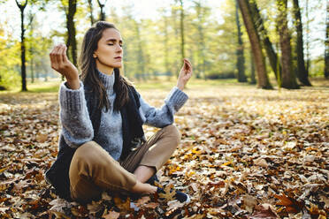 Young woman meditating in autumn forest - BSZF01712