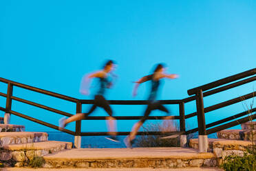 Seitenansicht von schlanken anonymen weiblichen Joggerin in Sportkleidung läuft auf alten Treppe mit Metallzaun in der Nähe von Meer unter heiteren Himmel - ADSF14402