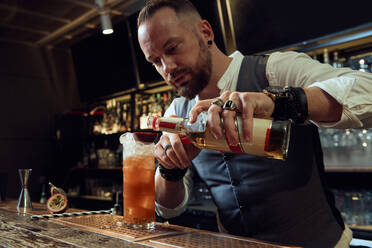 Professional young bartender holding bottle while preparing a cocktail in the bar - ADSF14434