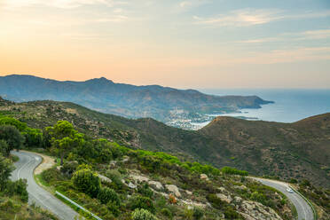 Von oben der wunderbaren Landschaft der Meeresküste mit kurvenreichen Straße führt durch felsige Berge und grünen Hügeln in der Nähe von Cadaques Stadt in Spanien im Sommer Abend mit bewölkten bunten Himmel im Hintergrund - ADSF14438