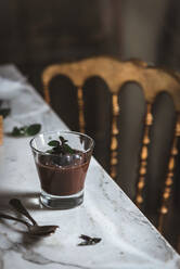 Still-life shoot of chocolate and mint mousse served inside glasses, placed on marble table against decorated background - ADSF14448