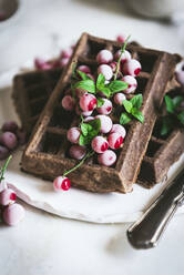 Von oben leckere frische Haferflocken-Schokowaffeln mit Stachelbeeren auf weißem Teller mit Löffel und Messer auf hellem Holztisch serviert - ADSF14450