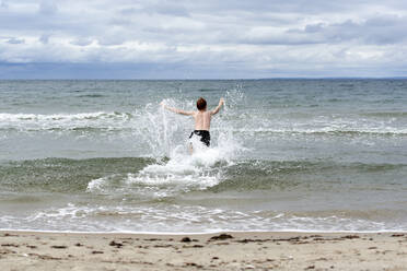 Shirtless boy enjoying splashing of water on beach - JEDF00331