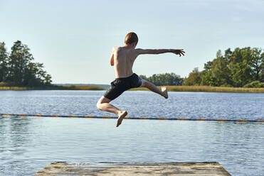 Redhead boy jumping into lake against clear sky - JEDF00335