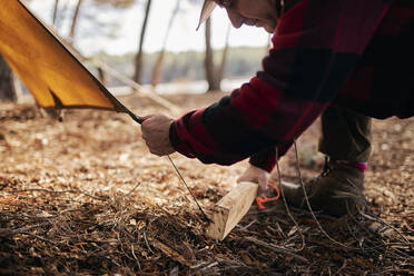 Midsection of bushcrafter preparing tent in forest - SASF00041