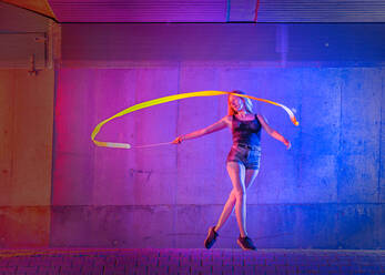 Woman spinning ribbon while dancing against wall - STSF02597