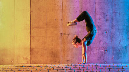 Frau übt Gymnastik in mehrfarbigem Licht an der Wand - STSF02603