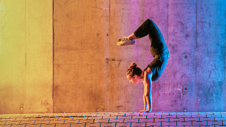 Woman practicing gymnastic in multi colored light against wall - STSF02603