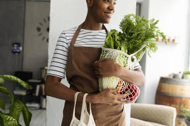 Pretty woman in apron carrying net with fresh vegetables - VABF03358