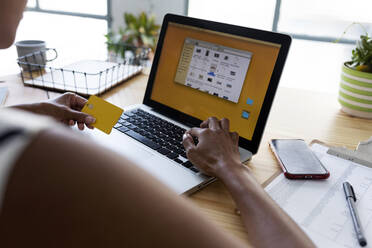 Businesswoman sitting in office using laptop to make an online payment with credit card - VABF03370