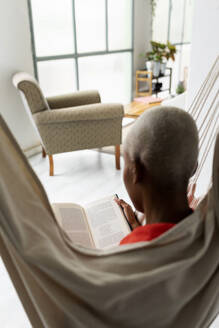 Frau sitzt in der Hängematte und liest ein Buch - VABF03395