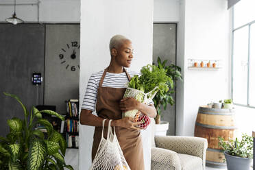 Pretty woman in apron carrying net with fresh vegetables - VABF03413