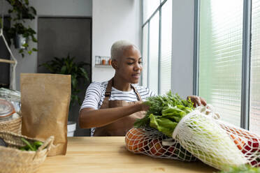 Woman with apron in kitchen , unpacking freshly bought organic fruit and vegetables - VABF03416