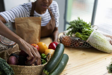 Frau mit Schürze in der Küche, beim Auspacken von frisch gekauftem Bio-Obst und -Gemüse - VABF03418