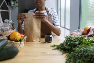 Frau mit Schürze in der Küche, beim Auspacken von frisch gekauftem Bio-Obst und -Gemüse - VABF03421