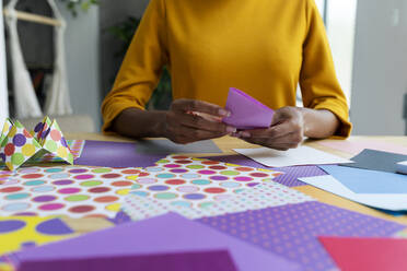 Origami artist sitting in studio folding colorful paper - VABF03432