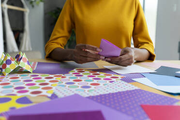Origami-Künstlerin sitzt im Atelier und faltet buntes Papier - VABF03432