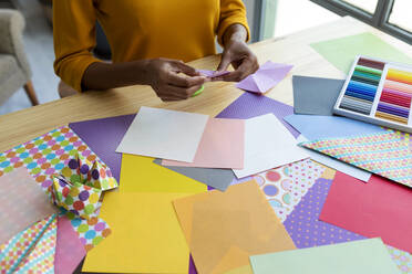 Origami-Künstlerin sitzt im Atelier und faltet buntes Papier - VABF03434