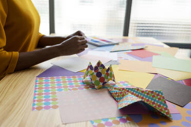 Origami artist sitting in studio folding colorful paper - VABF03435