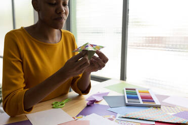 Origami-Künstlerin sitzt im Atelier und arbeitet mit buntem Papier - VABF03437