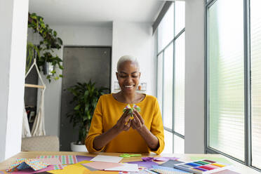 Origami artist sitting in studio working with colorful paper - VABF03438