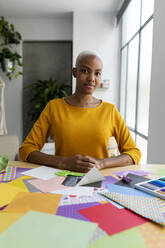 Origami artist sitting in studio with colorful papers - VABF03443