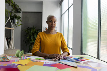 Origami artist sitting in studio with colorful papers - VABF03444