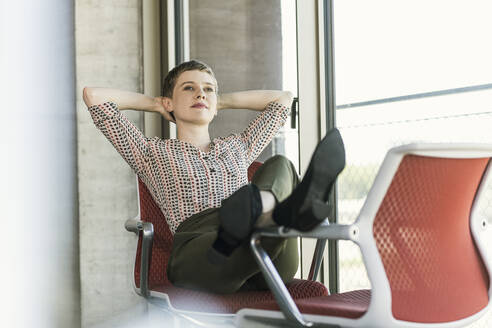 Entspannte Geschäftsfrau sitzt auf einem Stuhl im Büro und macht eine Pause - UUF21080