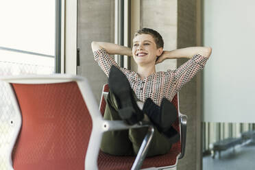 Lächelnde Geschäftsfrau, die auf einem Stuhl im Büro sitzt und eine Pause macht - UUF21081