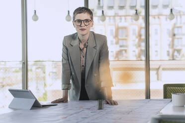 Portrait of confident businesswoman leaning on desk in office - UUF21090