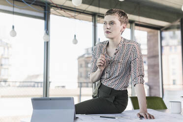 Thoughtful businesswoman sitting on desk in office - UUF21096