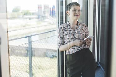 Businesswoman holding mobile phoneat the window in office - UUF21100