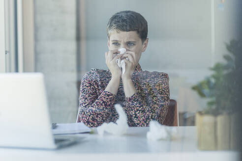 Kranke Geschäftsfrau am Schreibtisch im Büro beim Schnäuzen - UUF21109