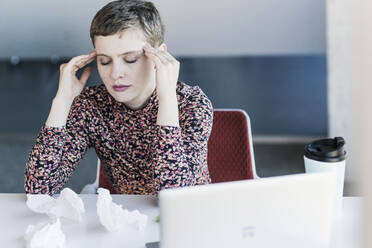 Geschäftsfrau am Schreibtisch im Büro mit Kopfschmerzen - UUF21116