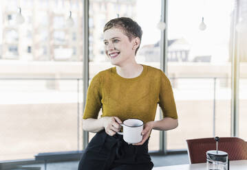 Lächelnde Geschäftsfrau im Büro mit Kaffeebecher in der Hand - UUF21125