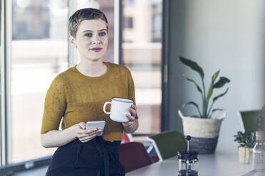 Geschäftsfrau im Büro mit Kaffeebecher und Mobiltelefon - UUF21132