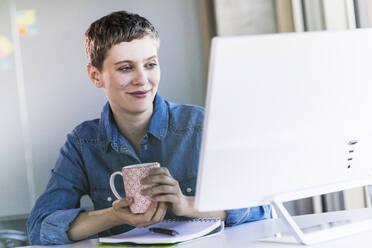 Smiling businesswoman at desk in office looking at computer screen - UUF21166