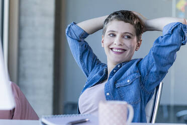 Smiling relaxed businesswoman sitting at desk in office - UUF21172